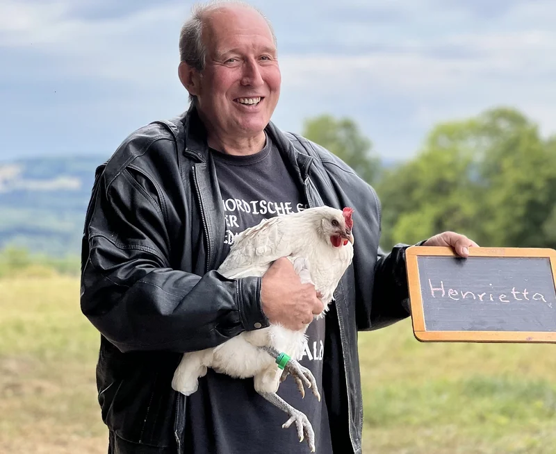 Mann mit Huhn auf dem Arm. Klick führt zu Großansicht in neuem Fenster.