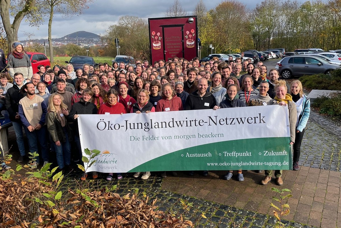 Viele jungen Menschen in einem Pulg. Sie schauen alle freundlich in die Kamera. Die Menschen in der ersten Reihe halten einen Banner hoch auf dem steht "Öko-Junglandwirte-Netzwerk". Klick führt zu Großansicht.