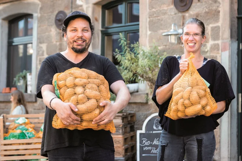 Mann und Frau halten jeweils einen Sack Kartoffeln in den Armen.