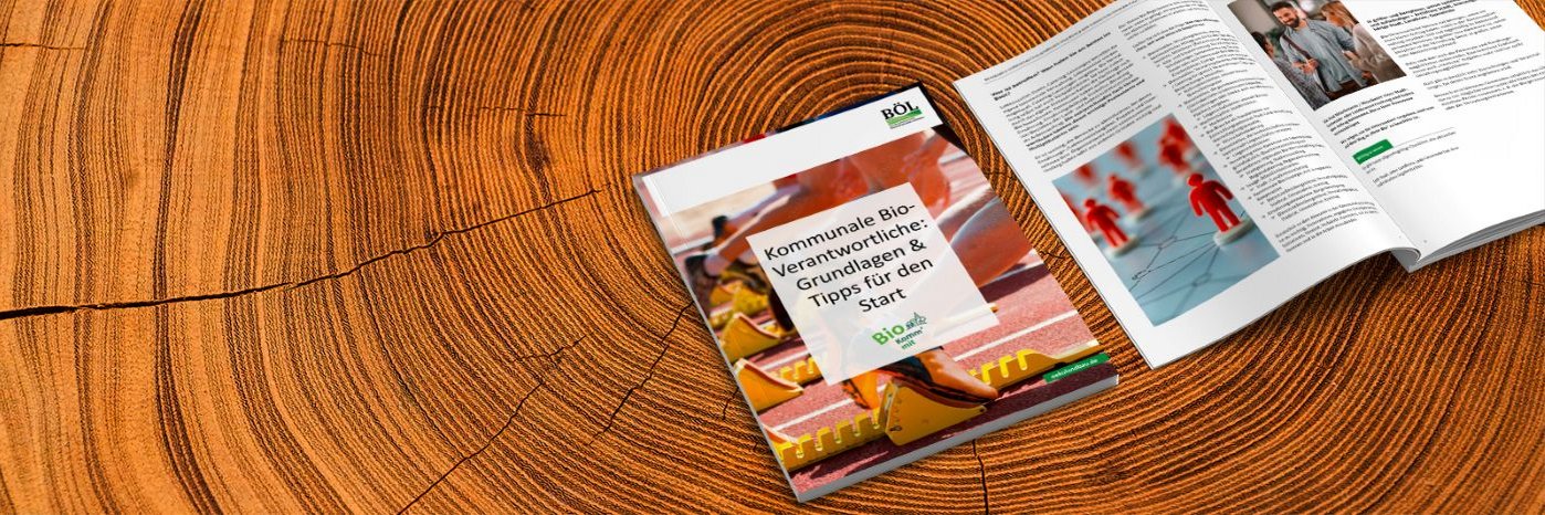 Zwei Broschüren von Bio Komm'mit auf einem Holztisch.