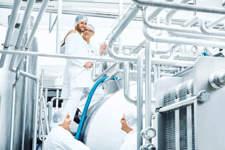 Molkereiproduktionsanlage mit Mitarbeitenden. Klick führt zu Großansicht im neuen Fenster.