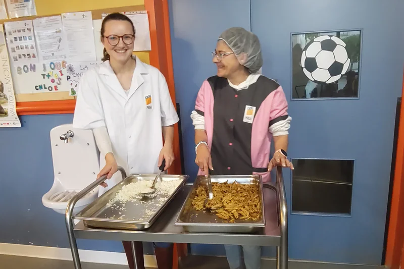 Mitarbeitenden in einer französischen Schulkantine in Levignac bei der Essensausgabe. Klick führt zu Großansicht in neuem Fenster.