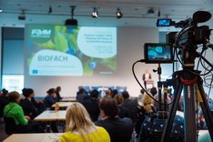 Blick auf eine Kamera, die während eines Vortrags auf der Biofach filmt. Klick führt zu Großansicht.