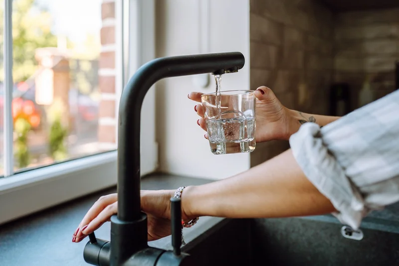 Eine Hand hält ein Trinkglas unter einen geöffneten Wasserhahn, aus dem klares Wasser in das Glas fließt. Klick führt zu Großansicht.