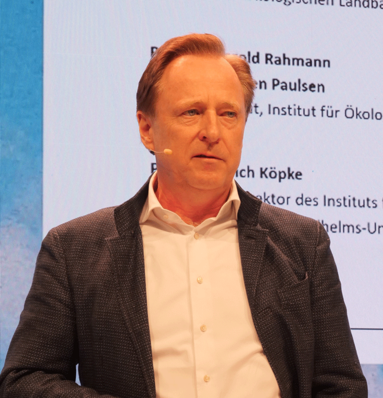Prof. Hülsbergen steht mit einem Headset-Mikro auf einer Bühne. Klick führt zu Großansicht in neuem Fenster.