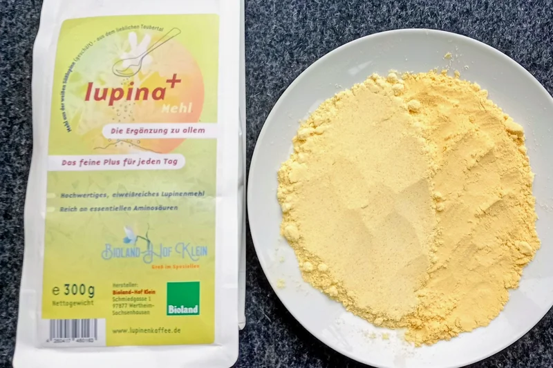 Blick auf eine Packung Lupinenmehl. Daneben befindet sich ein Schälchen mit Lupinenmehl. Klick führt zu Großansicht.