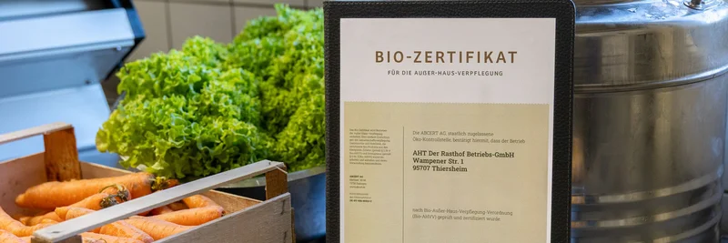 Bio-Zertifikat neben einer Kiste Möhren und Bund Salat.