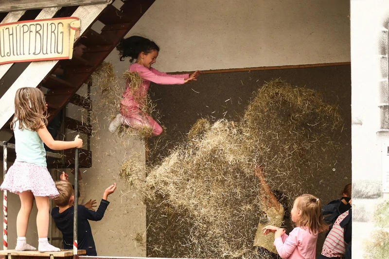Mädchen hüpft ins Heu. Klick führt zu Großansicht in neuem Fenster.