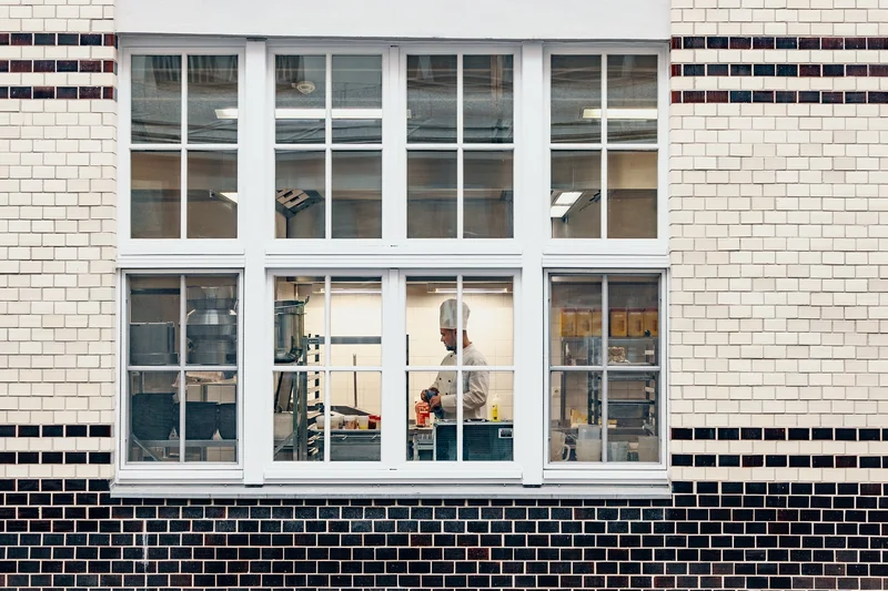 Blick durch ein Fenster auf einen Koch, der in einer Großküche arbeitet.