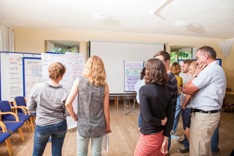 Menschen in einem Raum vor Pinnwänden.