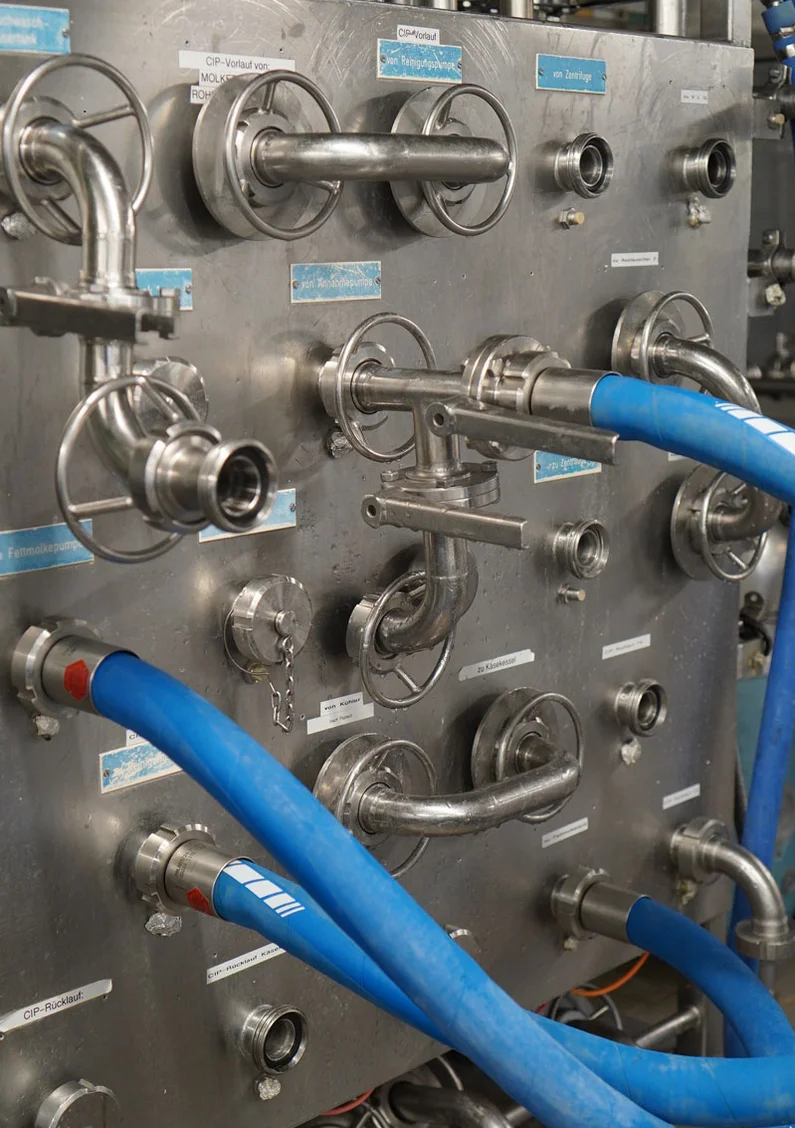 Rückwand eines Pasteurisators mit zahlreichen Ventilen und blauen Schläuchen.