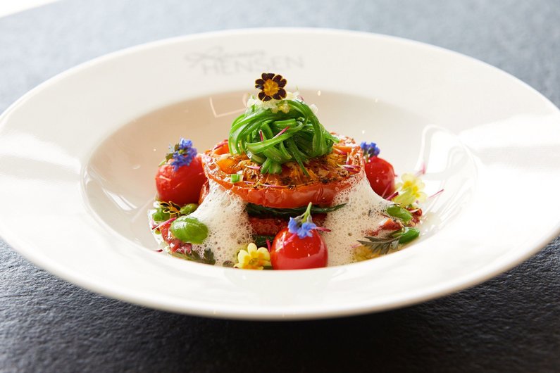 Mille Feuille von Ochsenherztomaten, Bohnen, Spinat und Erbsen mit weißem Tomatenschaum auf einem Teller angerichtet.