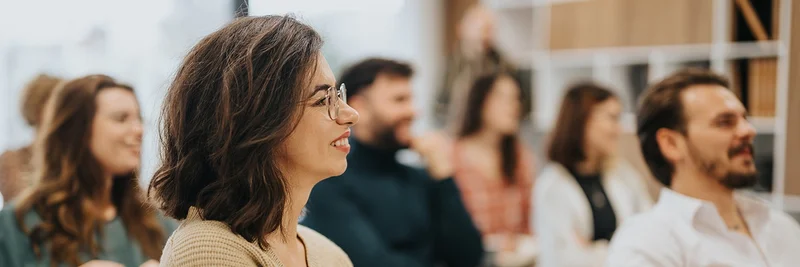 Viele Menschen in einem Hörsaal. Eine Frau mit Brille ist im Fokus.