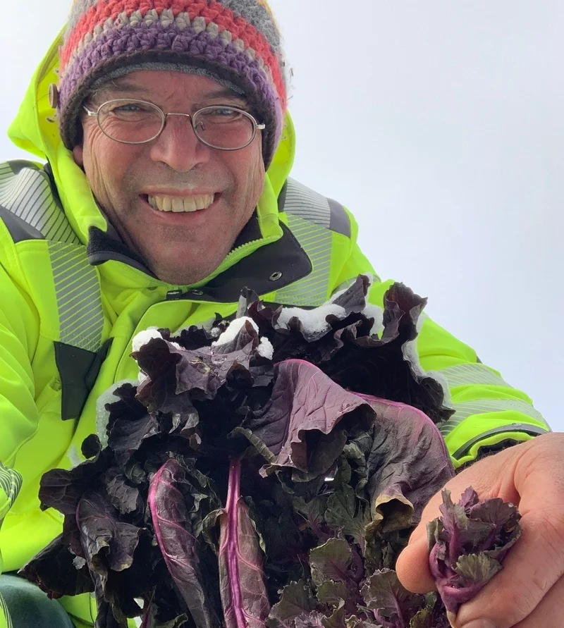 Mann mit Mütze hält Rosenkohl Sprouts in die Kamera. Klick führt zu Großansicht in neuem Fenster, schließen per ESC.