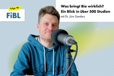 Ein Mann sitzt vor einem Mikrofon und schaut freundlich in die Kamera. Klick führt zu Großansicht.