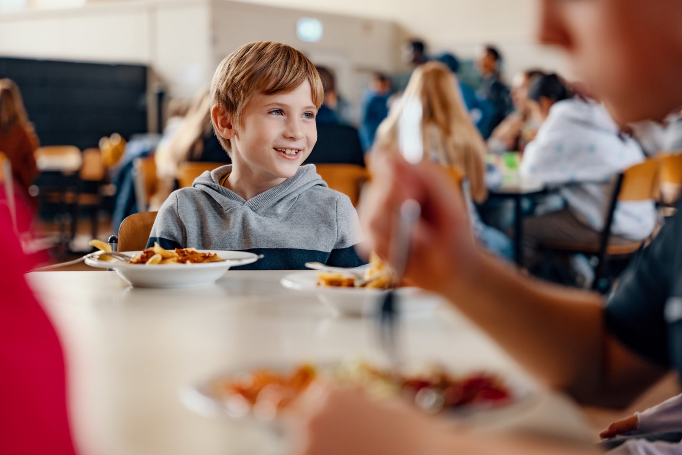 Junge sitzt in der Kantine mit Nudelgericht auf dem Tisch.