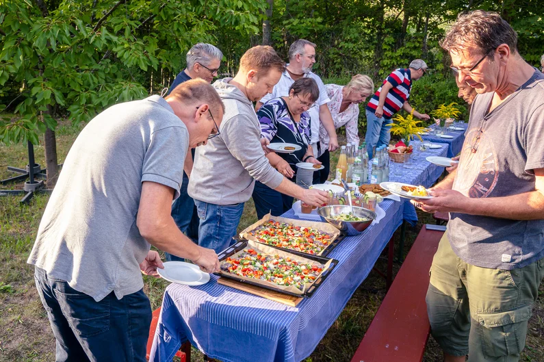 Mehrere Menschen stehen um einen gedeckten Tisch in einem Garten und bedienen sich am Buffet.
