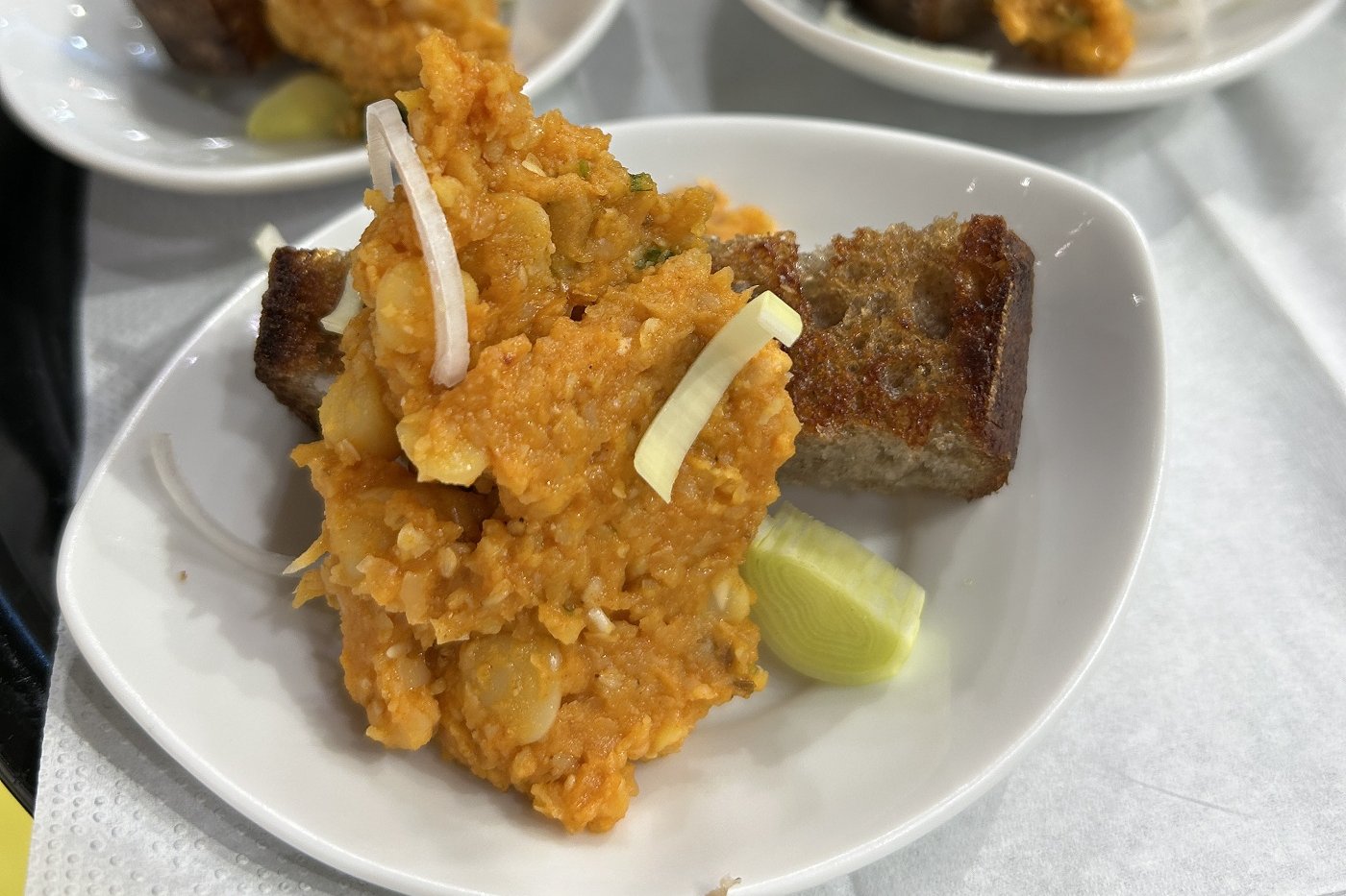 Gelber Erbsenhummus mit geröstetem Landbrot und Olivenöl angerichtet auf kleinen Tellern.
