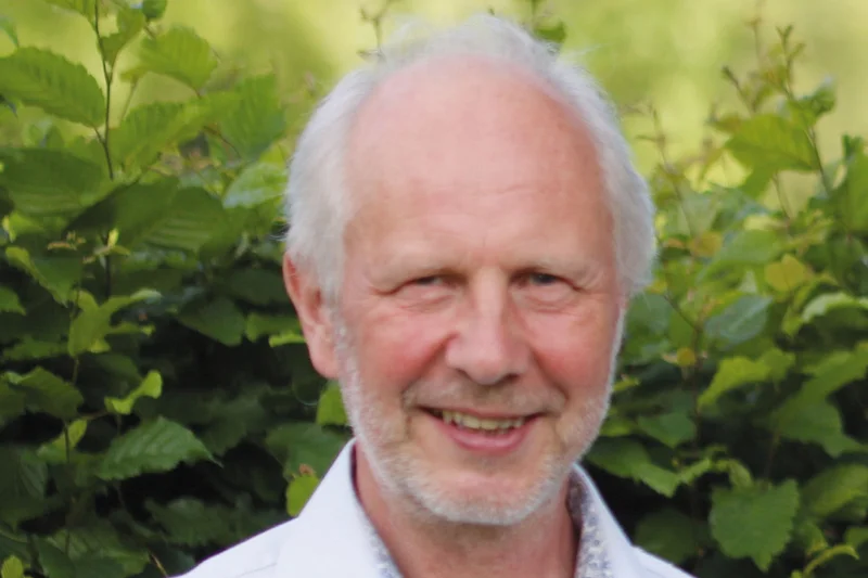 Man steht vor einer grünen Hecke und lacht in die Kamera. Klick führt zu Großansicht.