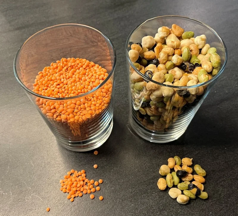 Erbsen-Bohnen-Mischung und rote Linsen in einem Glas und vor dem Glas.