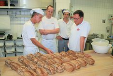 Vier Bäcker stehen an einem Tisch voller Brote.