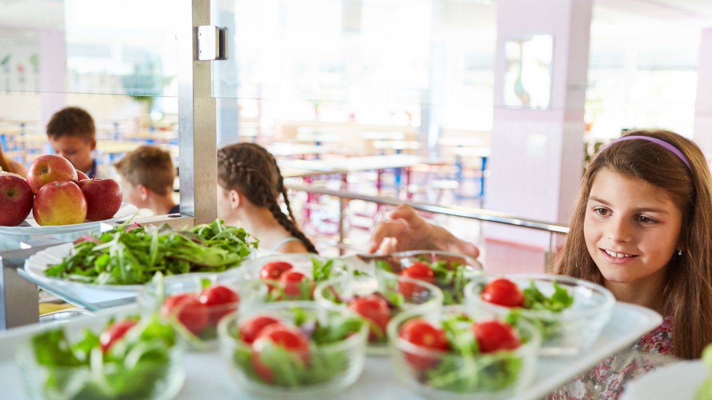 Mädchen nimmt sich in der eine Schüssel Salat in einer Schulkantine. 