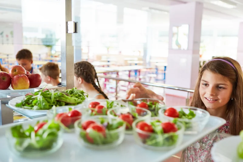 Mädchen nimmt sich in der eine Schüssel Salat in einer Schulkantine. 