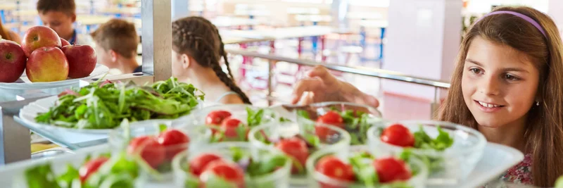 Mädchen nimmt sich eine Schüssel Salat in der Schulkantine.