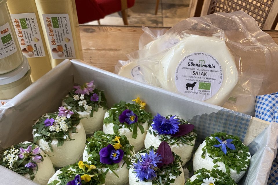 Käse mit Blüten geschmückt in einer Kiste. Klick führt zu Großansicht.