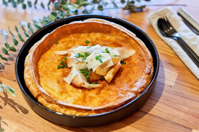 Dutch Baby mit Zwetschgenröster und Ziegenfrischkäse angerichtet in einer Kuchenform.