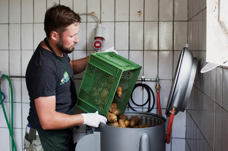Biolandwirt Dominik Heitzer mit Kartoffelschälmaschine. Klick führt zu Großansicht im neuen Fenster.