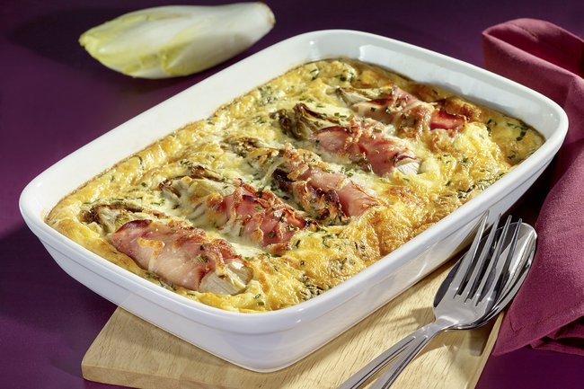 Überbackener Chicorée mit Kochschinken und Bergkäse in einer Auflaufform.