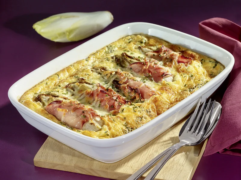 Überbackener Chicorée mit Kochschinken und Bergkäse in einer Auflaufform.
