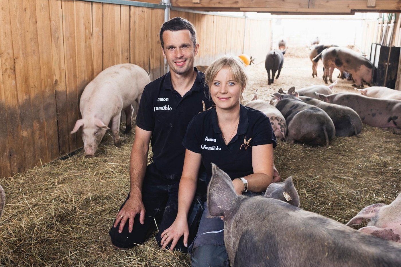 Eine Frau und ein Mann kniend in einem Schweinestall. Klick führt zu Großansicht.