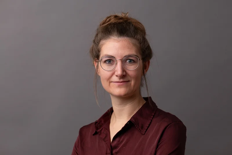 Frau mit Brille lacht in Kamera. Klick führt zu Großansicht.