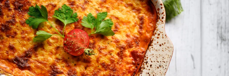 Auflaufform mit goldbraunem Gratin, garniert mit Tomaten und Basilikum.