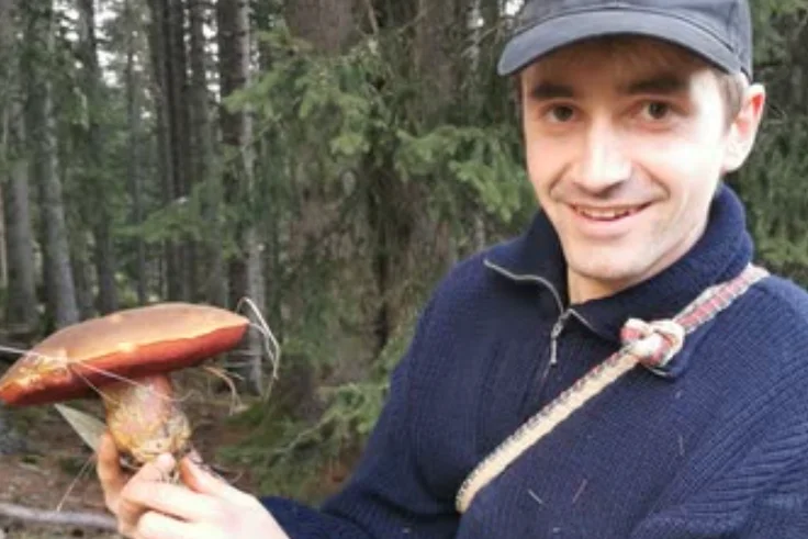 Junger Mann im Wald mit Pilz in der Hand. Klick führt zu Großansicht.