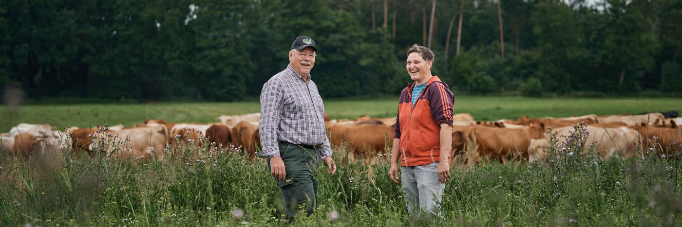 Mann und Frau lachen auf einer Rinderweide.