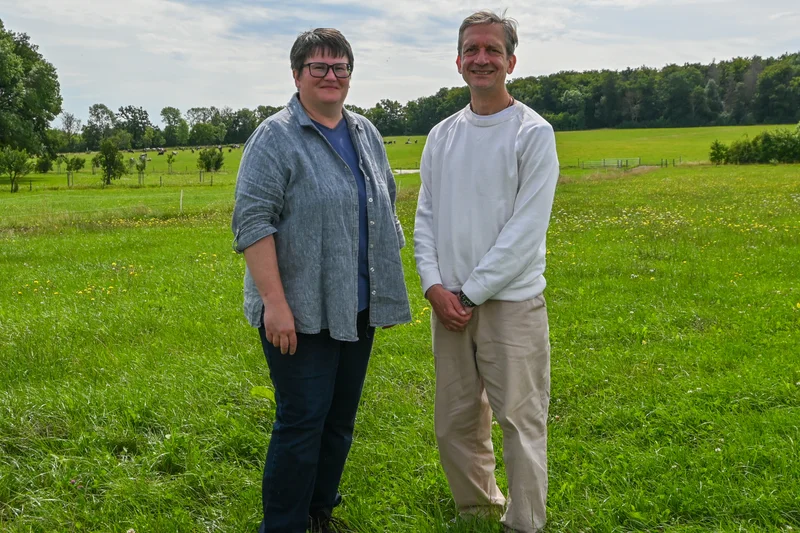 Eine Frau (links) und ein Mann (rechts) stehen auf einem Feld nebeneinander und schauen freundlich in die Kamera. Klick führt zu Großansicht.