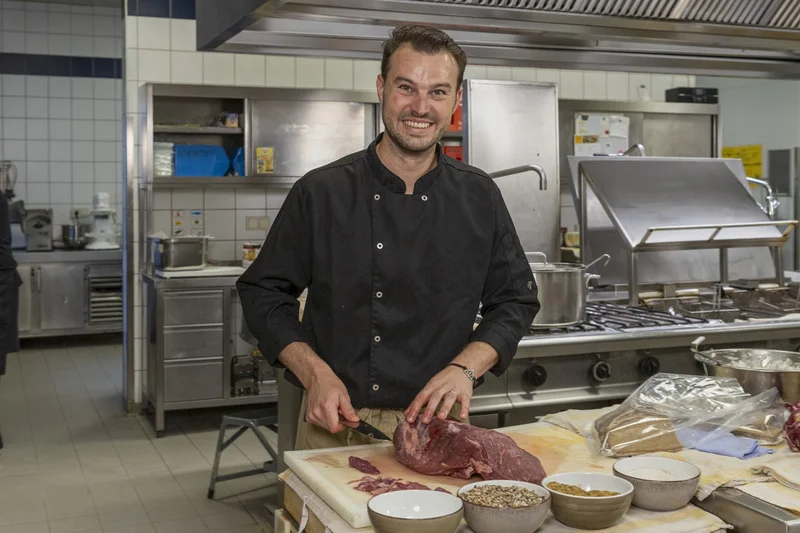 Koch schneidet Fleisch. Klick führt zu Großansicht in neuem Fenster, schließen per ESC.