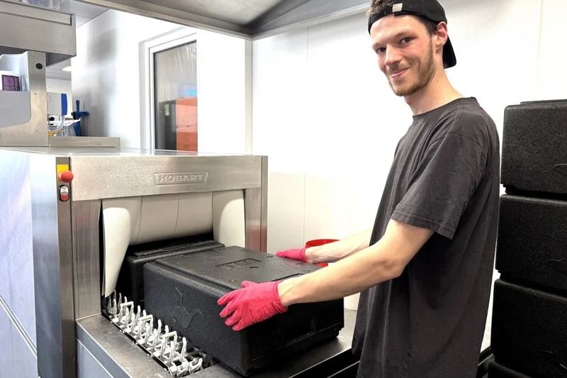 Junger Mann reinigt Transportkiste. Klick führt zu Großansicht.