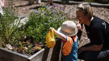 Kita-Kind und Betreuerin am Hochbeet