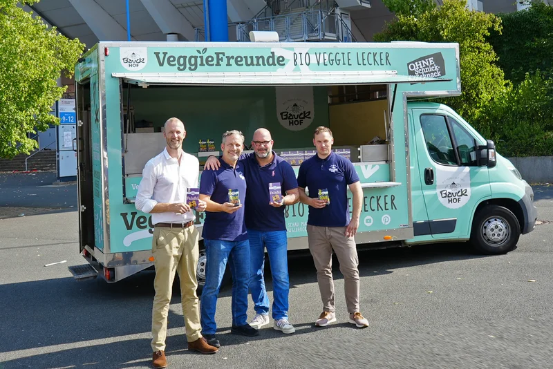 Vier Männer vor einem Foodtruck, die in die Kamera lächeln.