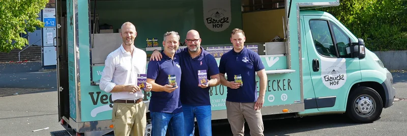 Vier Männer vor einem Foodtruck, die in die Kamera lächeln.