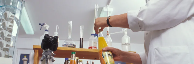 Eine Frau entnimmt in einem Labor Proben aus einer Saftflasche.