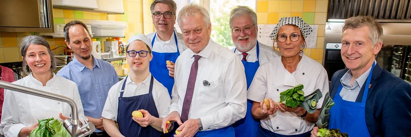 Menschen in einer Küche mit Gemüse in der Hand. Sie schauen alle freundlich in die Kamera.