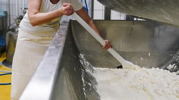Eine Frau in einer Molkerei beim Käse rühren.