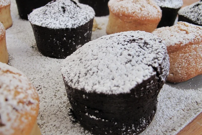 Schokoladenmuffin auf einem Backblech mit Puderzucker bestäubt. Klick führt zu Großansicht in neuem Fenster.