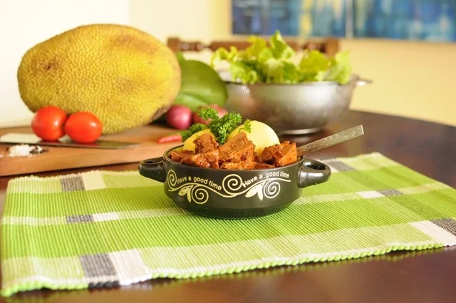 Veganes Gulasch aus Jackfrucht und Kartoffeln, unverarbeitete Jackfrucht im Hintergrund. Klick führt zu Großansicht im neuen Fenster.
