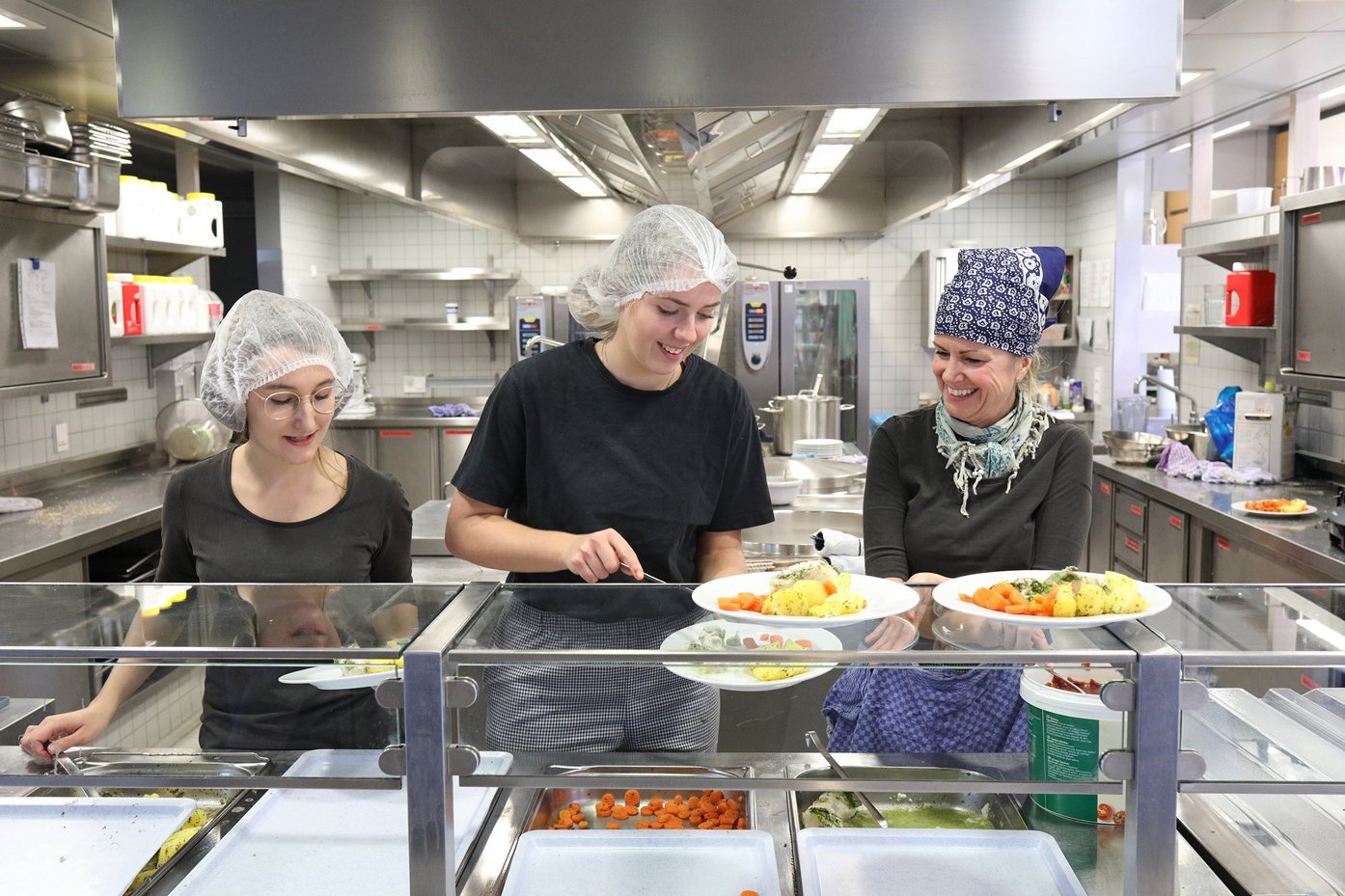 Drei Frauen bei der Speiseausgabe an der Theke einer Großküche. Foto: Bernd Wackerbauer